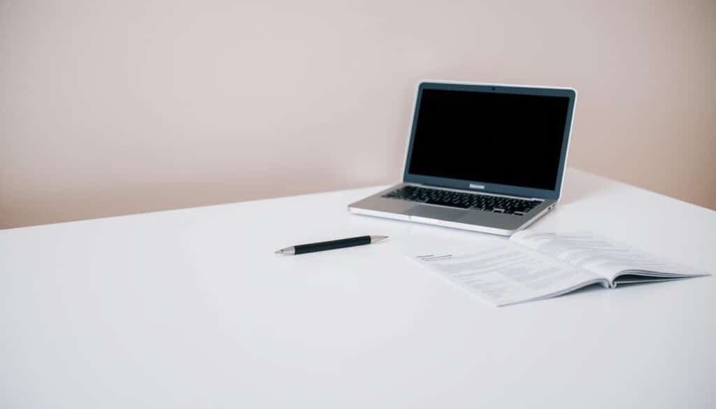 A high-quality, detailed image of a minimalist desk setup depicting the criteria for choosing a competent cosmetic surgeon. The desk has a clean, modern design with a laptop, pen, and medical documents arranged neatly. The background is a soft, neutral-toned wall, creating a professional, clinical atmosphere. Soft, directional lighting illuminates the scene, highlighting the key elements. The overall mood is one of thoughtfulness, research, and attention to detail, reflecting the important decision of selecting a qualified cosmetic surgeon.